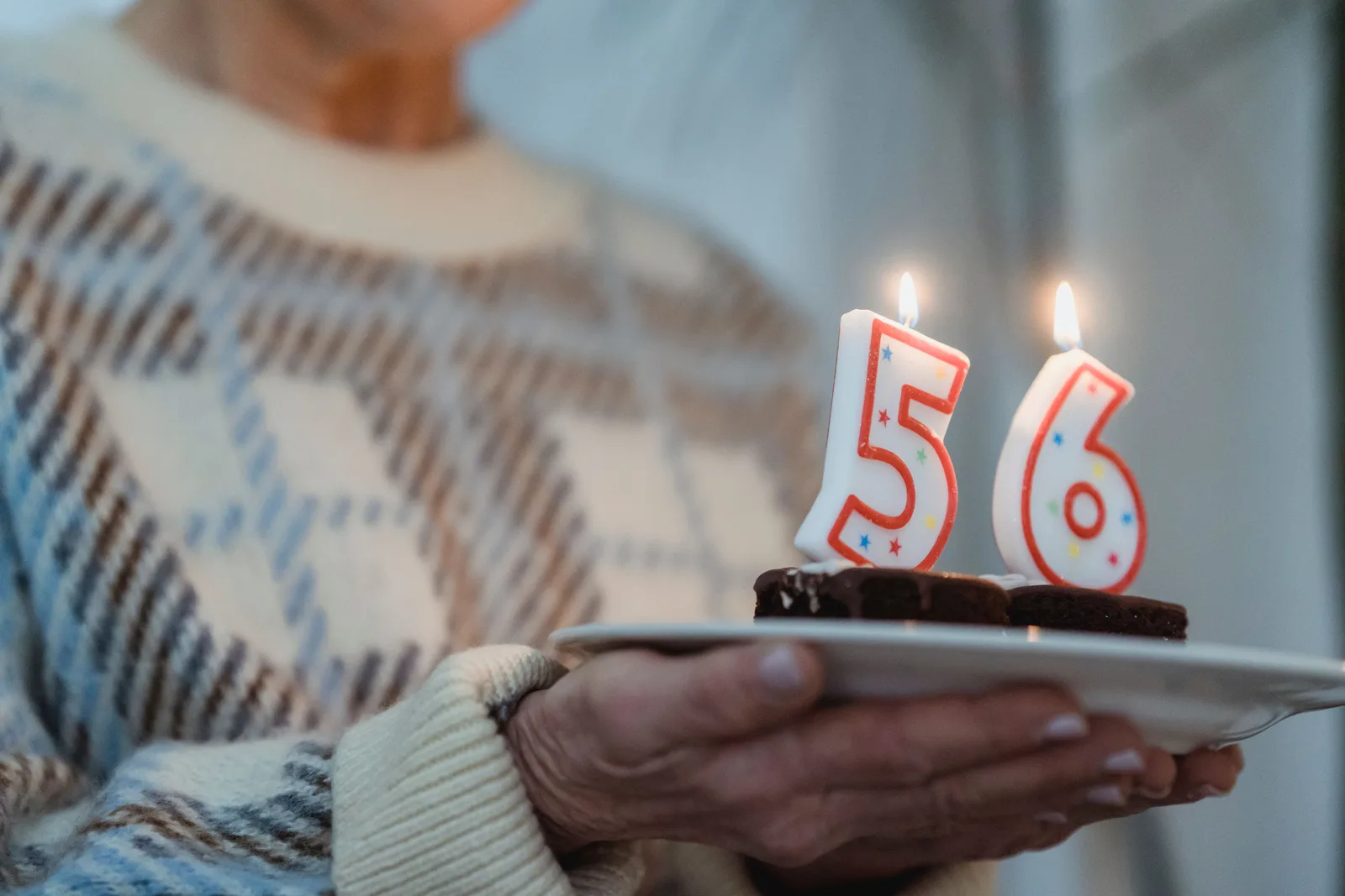 Person holding a birthday cake with number 56 candles