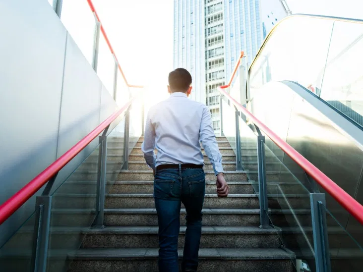 A person climbing outdoor stairs beside an escalator
